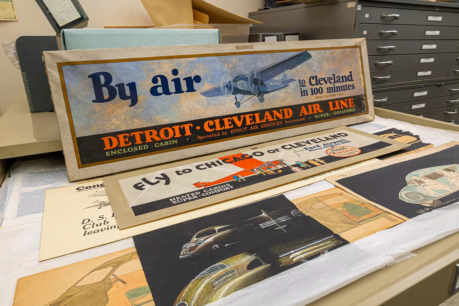 Vintage airline posters and brochures on a tabletop, highlighting Detroit-Cleveland Air Line in vibrant colors.
