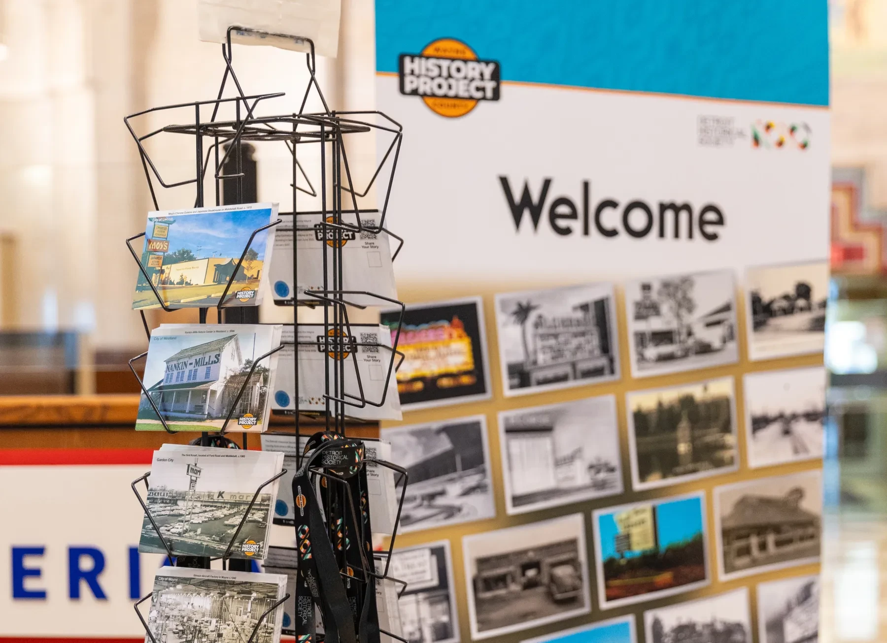 Postcard rack in front of a "Welcome" exhibit sign with historical photos.