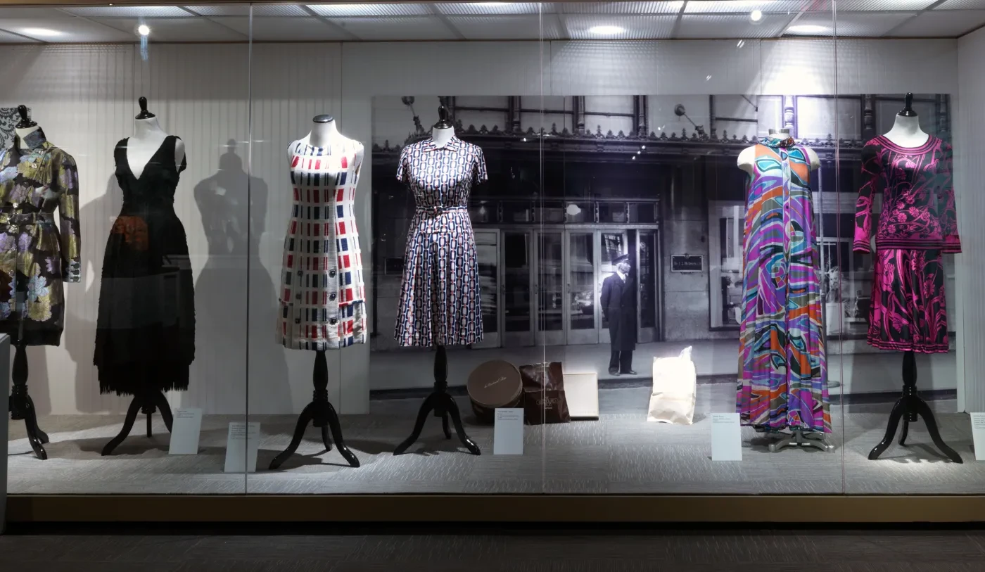 Five mannequins in a store display, each wearing a colorful, patterned dress under soft lighting.