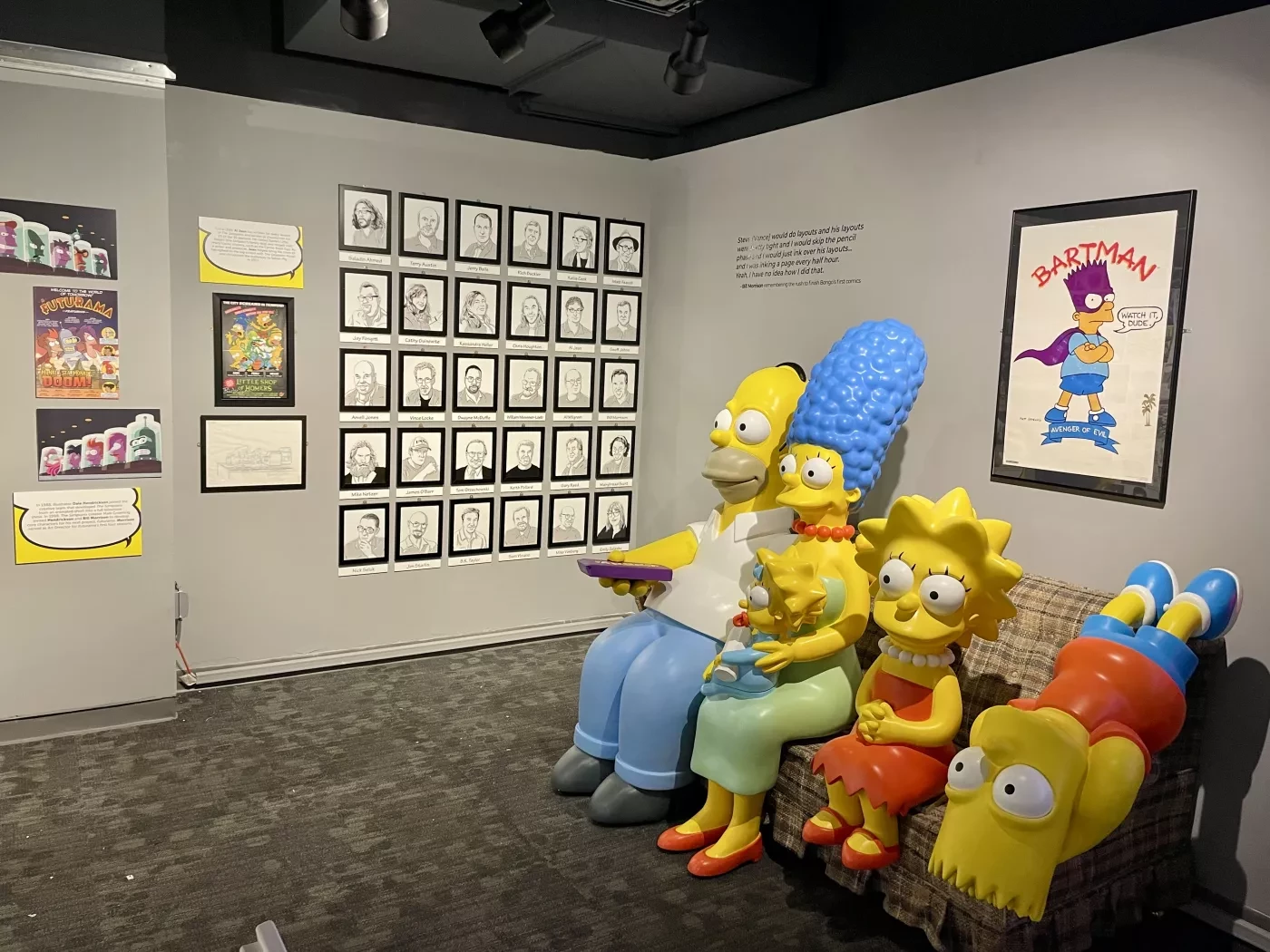 Exhibit featuring life-size Simpsons sculptures on a couch with framed sketches on the walls.