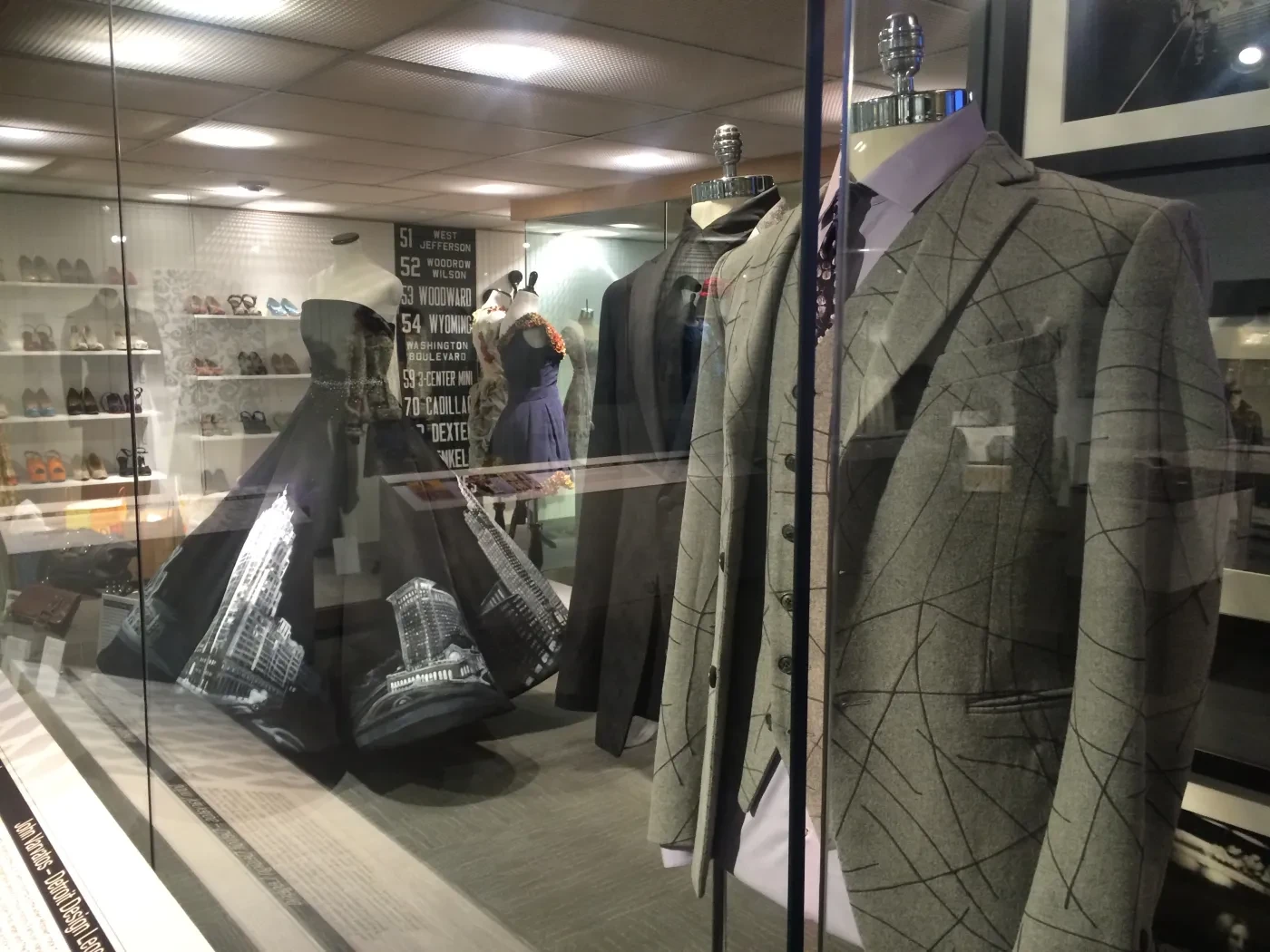 Storefront displaying mannequins in tailored gray suits with geometric patterns and other garments in the background.