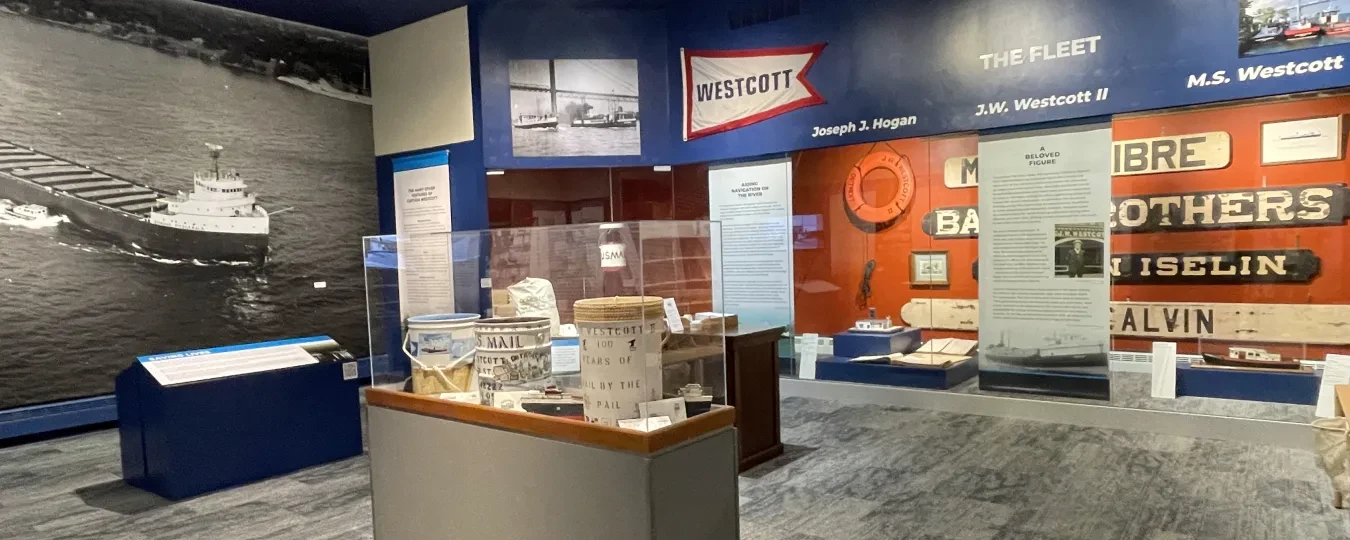 Museum exhibit room with nautical-themed displays, model ships, and historical photos on the blue and red walls.