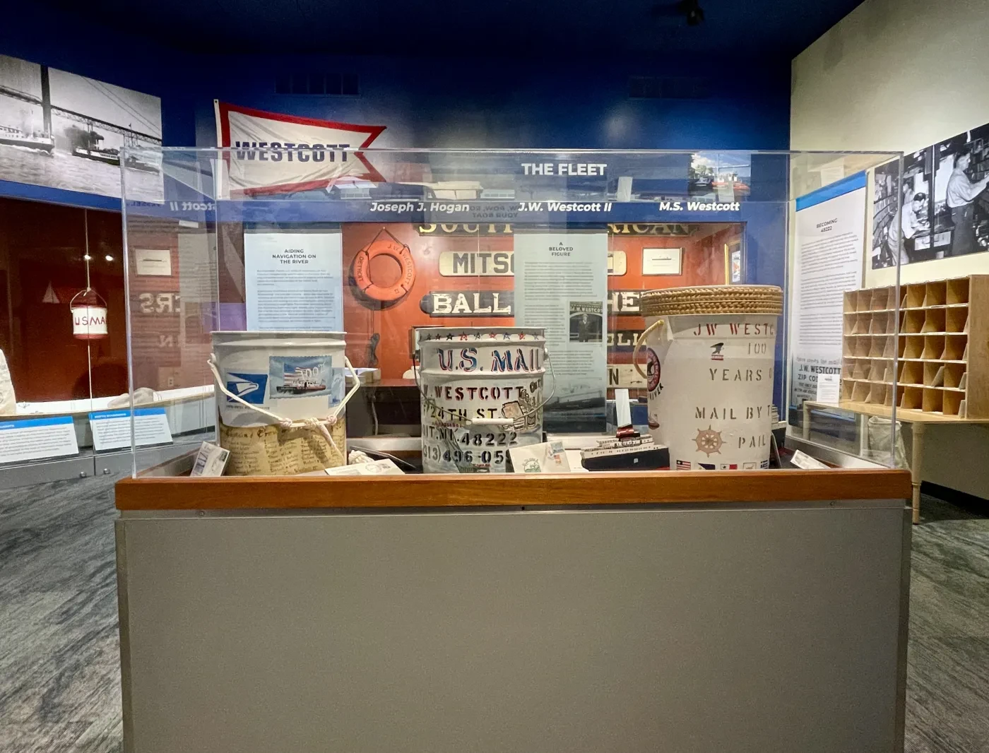 Museum exhibit with vintage Navy canisters and posters on display, inside a glass case.