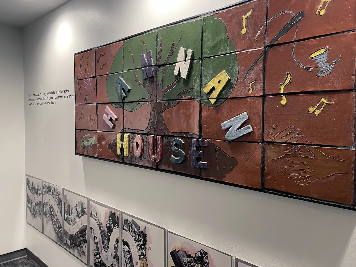 Mural with colorful tiles spelling out a name, surrounded by musical notes on a hallway wall.