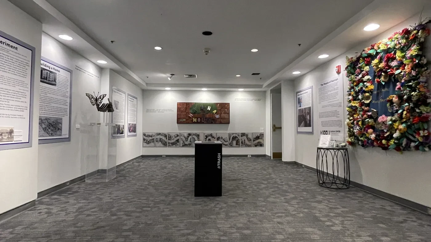 Museum hallway with colorful artwork and informational panels on white walls, with a central black pedestal.