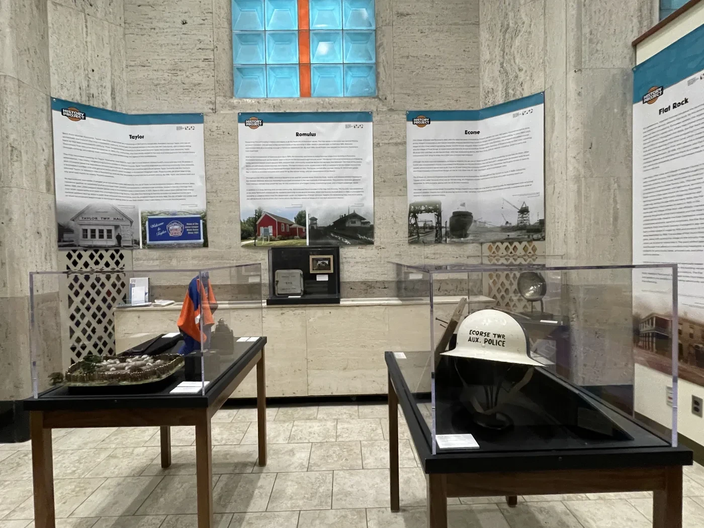 Museum exhibit with artifacts in glass cases, informational panels on walls, and a large display window above.