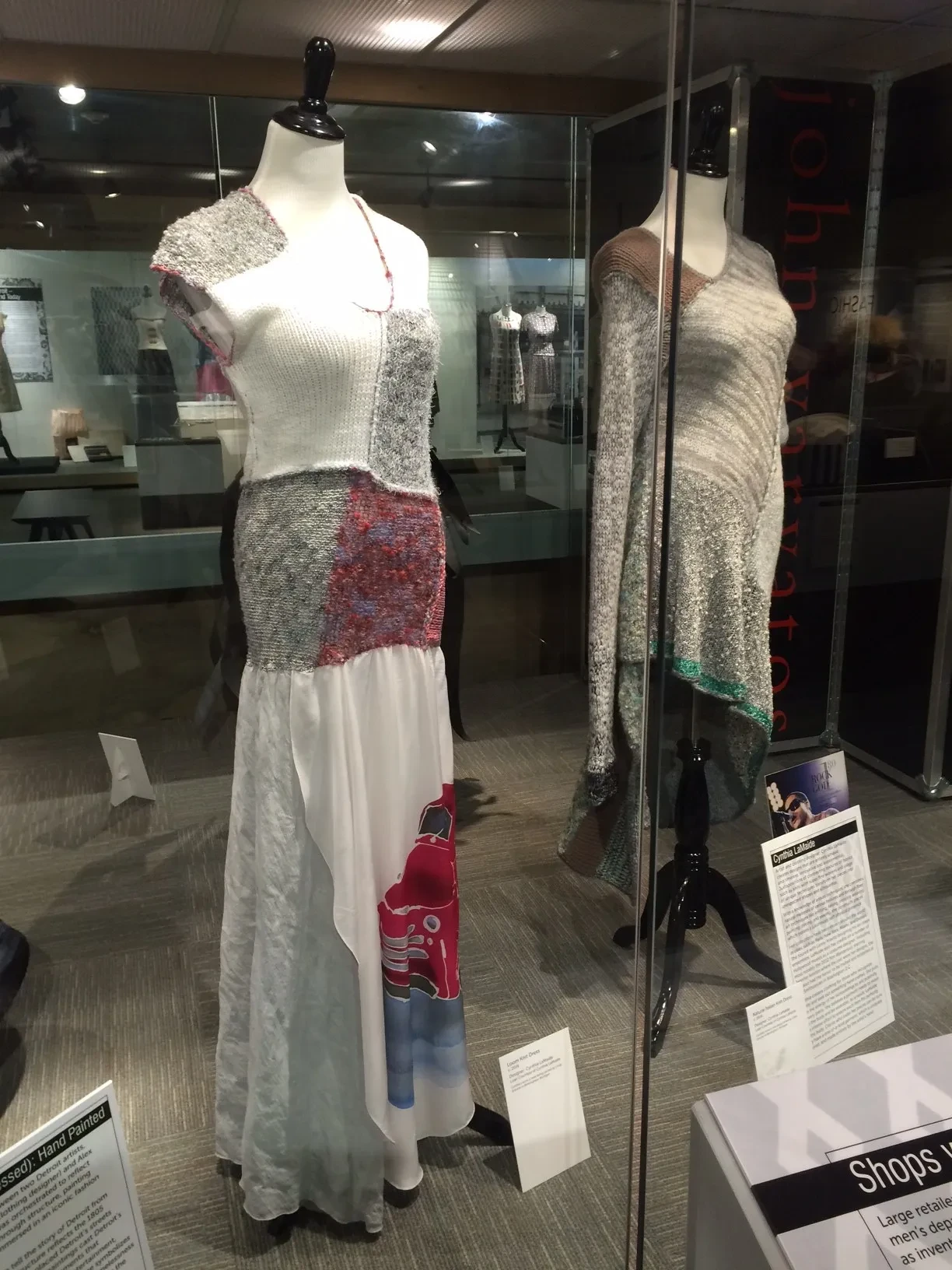 Two mannequins display colorful patchwork dresses in a museum exhibit, with informational plaques nearby.