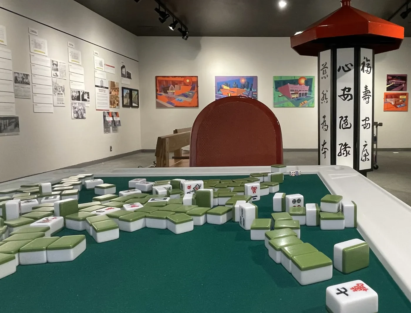 Mahjong pieces scattered on a table in an art gallery with colorful paintings on the walls.